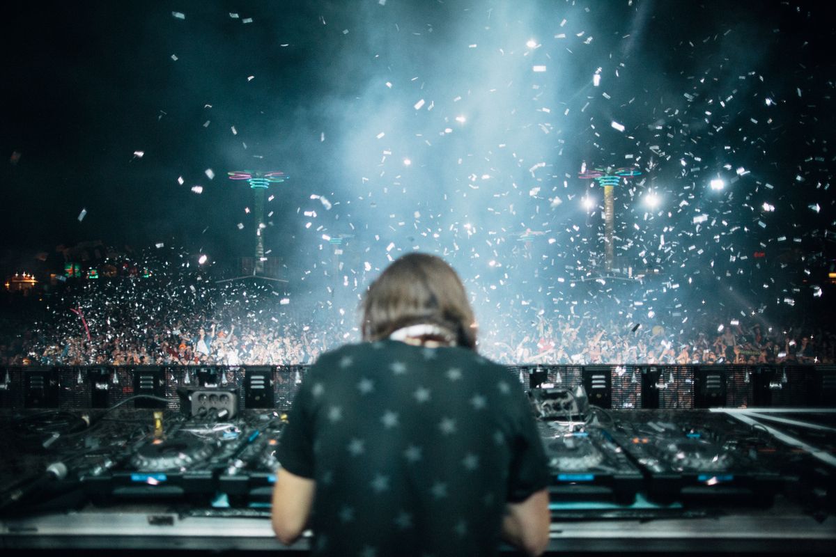 DJ a tančící festivalové publikum pod modrými světly a konfetami